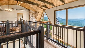 A spacious loft with a high ceiling, exposed wooden beams, a stone wall, and large windows offering mountain views. - Wow Wow Wow a must stay cabin! (Sevierville)