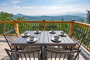 A wooden deck with a table set for six, surrounded by metal chairs, overlooking a mountainous landscape. - Wow Wow Wow a must stay cabin! (Sevierville)