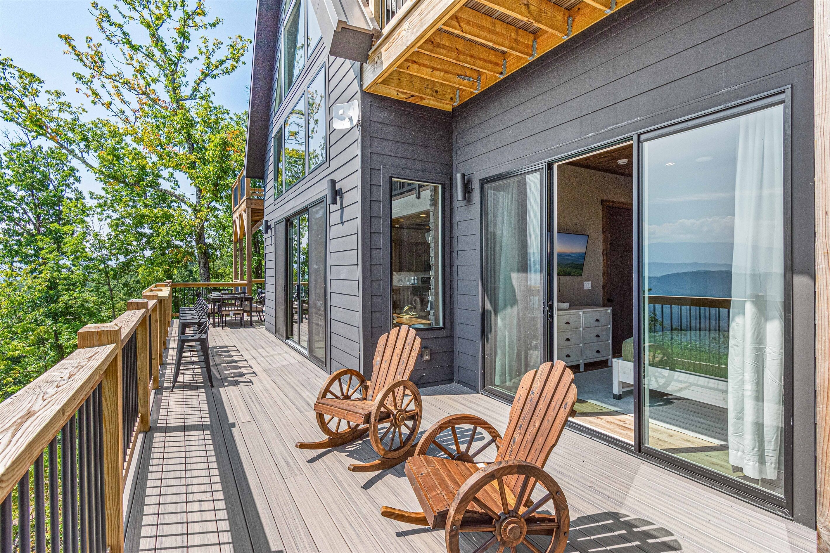 A deck with wooden chairs and a table, overlooking a scenic view.