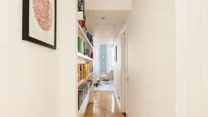 A hallway with bookshelves, a framed picture, and a door leading to a room with a chair. - Sugared Almond - 1 bedroom apartment Notting Hill (Greater London)