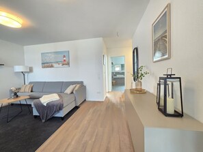 Uma sala de estar moderna com um sofá cinzento, uma mesa de centro, um abajur e um quadro de um farol.