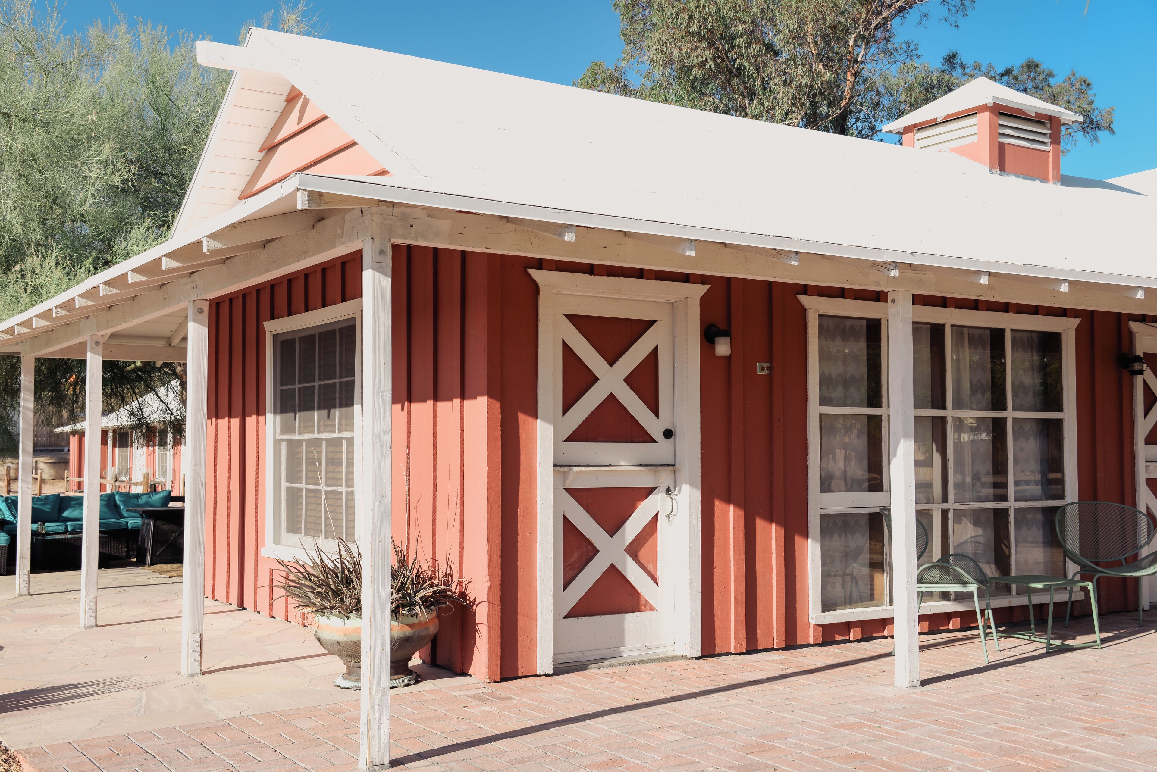 A red building with a white door and windows, a covered patio area, and outdoor seating.