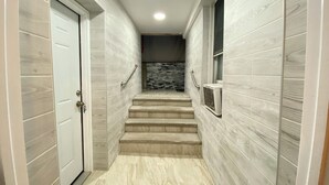 A hallway with a door on the left, a window on the right, and a set of stairs leading to a room with a tiled wall. - Nice two Bedroom apt at 25 Minutes to New York (North Bergen)