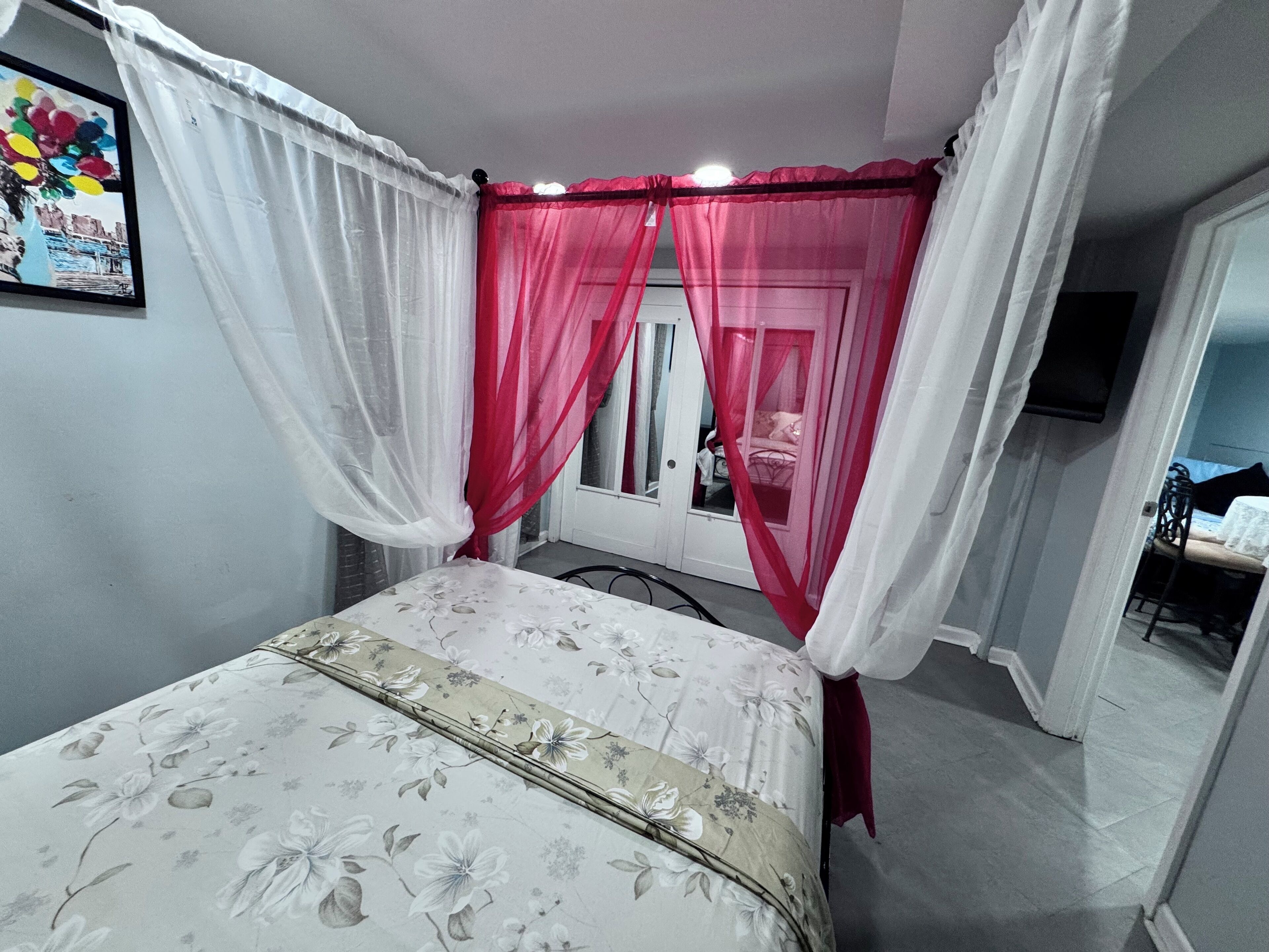 Ein Schlafzimmer mit einem Bett, einem Fenster mit Spiegel und einer Tür zu einem weiteren Raum.