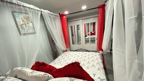 A bedroom with a bed, white and red curtains, and a view of a cityscape through a window. - Nice two Bedroom apt at 25 Minutes to New York (North Bergen)