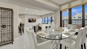 Un comedor moderno con una mesa de vidrio, sillas blancas y vistas a la ciudad a través de amplias ventanas.