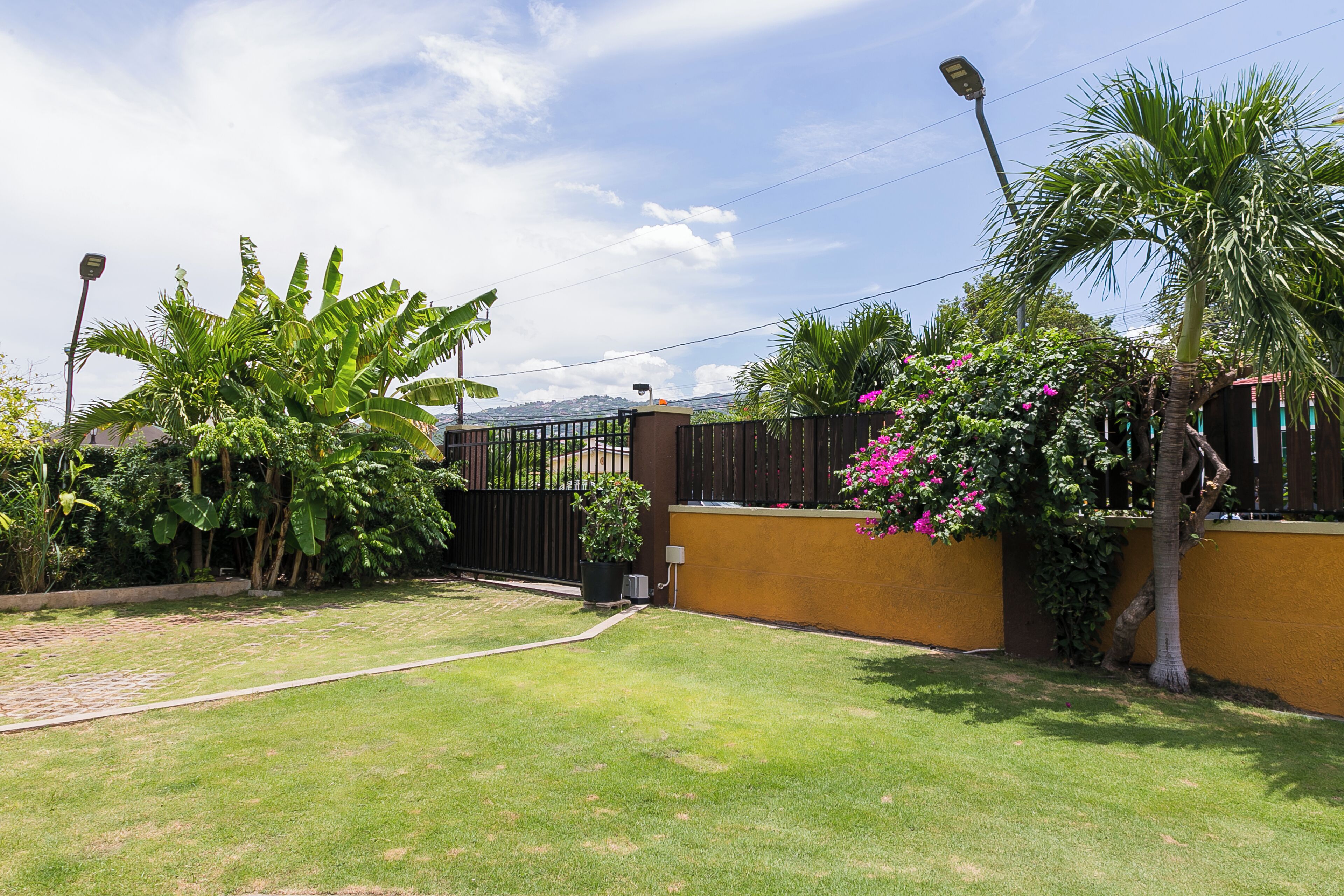 A well-maintained garden with a paved pathway, a black metal gate, and a yellow wall.