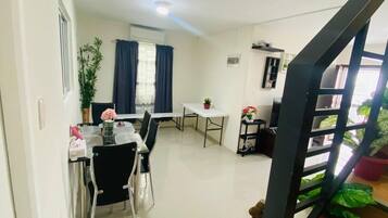 A dining area with a table and chairs, a small white table, and a potted plant.