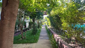 A pathway lined with trees and greenery, leading to a building with a tiled roof. - Villa Phum Khnar (Siem Reap)