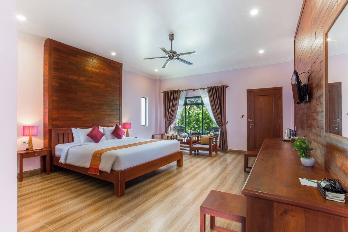 Ein Schlafzimmer mit einem hölzernen Bett, einem Schreibtisch, einem Stuhl, einem Deckenventilator und einem Fenster mit Vorhängen.