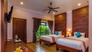 A hotel room with two beds, a ceiling fan, a TV mounted on the wall, a window with curtains, and a fruit basket on the floor. - Villa Phum Khnar (Siem Reap)