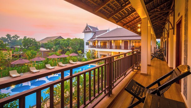 A balcony with a pool, lounge chairs, and umbrellas overlooking a resort area. - Villa Phum Khnar (Siem Reap)