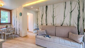Una sala de estar moderna con un sofá color beige, una mesa de comedor con sillas y una pared con diseño de árbol.