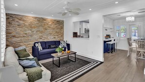 Un salon moderne avec un mur d’accent en pierre, un canapé bleu, un canapé blanc et une table basse agrémentée d’un vase et d’oranges.