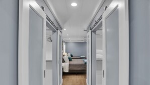 Un couloir étroit, avec un lit au fond, un plancher en bois et des murs blancs.