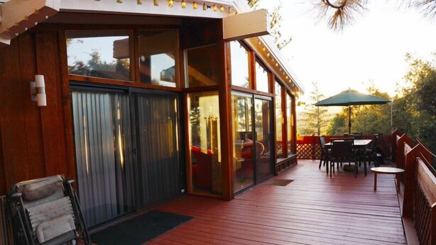 A wooden deck with a glass enclosure, outdoor seating, and a view of the surrounding area. - 3-Bedrooms in Idyllwild - AC, 
Jacuzzi, Sauna, Fitness-Game Room,  Epic Views (Idyllwild)