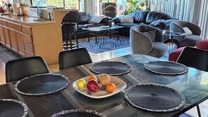A modern kitchen with a dining area, featuring a large glass table with black placemats and a fruit plate. - 3-Bedrooms in Idyllwild - AC, 
Jacuzzi, Sauna, Fitness-Game Room,  Epic Views (Idyllwild)