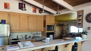 A modern kitchen with wooden cabinets, stainless steel appliances, a central island with bar stools, and various kitchen items. - 3-Bedrooms in Idyllwild - AC, 
Jacuzzi, Sauna, Fitness-Game Room,  Epic Views (Idyllwild)
