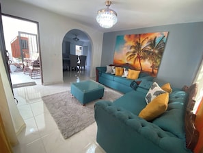 A living room with a sofa, ottoman, and a painting of palm trees. - 6B Santiago Harmonic Apt Especially For You (Santiago de los Caballeros)