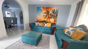 A living room with a sofa set, a glass coffee table, and a painting of palm trees. - 6B Santiago Harmonic Apt Especially For You (Santiago de los Caballeros)
