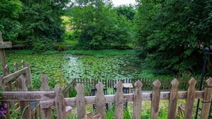 A wooden deck with a view of a pond surrounded by lush greenery. - No 27 A. Field - Coghurst Hall Hastings (Hastings)