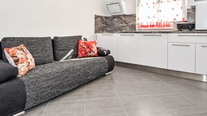 Una cocina moderna con armarios blancos, piso de baldosas grises y un sofá gris con cojines estampados.