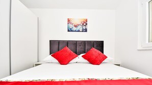 Un dormitorio moderno con una cama, dos almohadas rojas, un cabecero gris y una colcha estampada con motivos florales.