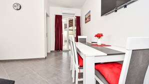 Una habitación moderna y luminosa con una mesa de comedor blanca, cojines rojos y un televisor montado en la pared.
