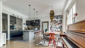 Une cuisine moderne dotée d’un îlot central, un coin repas avec une table ronde et des chaises, un piano et une bibliothèque remplie de livres.