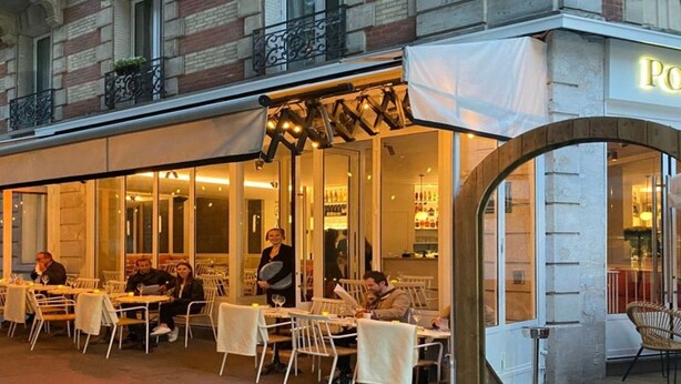 Un espace extérieur aménagé pour les repas, avec des tables et des chaises, un coin salon abrité et une entrée bien visible menant à l’intérieur du restaurant.
