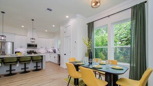 Una cocina moderna con armarios blancos, una isla central y un comedor con sillas amarillas y una mesa preparada para cuatro.