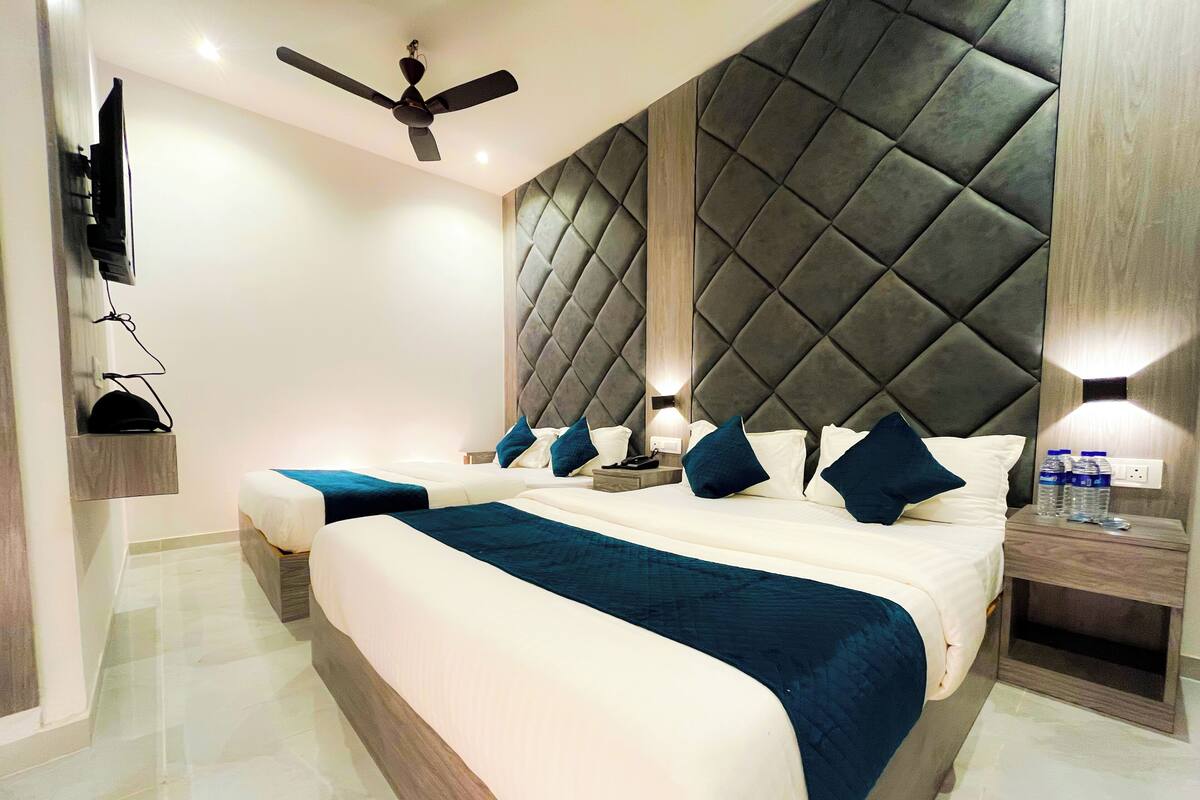 Une chambre d’hôtel moderne dotée d’un grand lit, d’un ventilateur de plafond, d’un téléviseur fixé au mur et d’une table de chevet avec une lampe et des bouteilles d’eau.