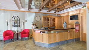 A reception area with a wooden counter, two red chairs, a clock, and a wall-mounted wine rack. - Appartements Robert Bechlwirt (Kirchberg in Tirol)