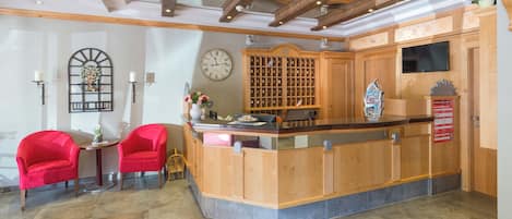A reception area with a wooden counter, two red chairs, a clock, and a wall-mounted wine rack.