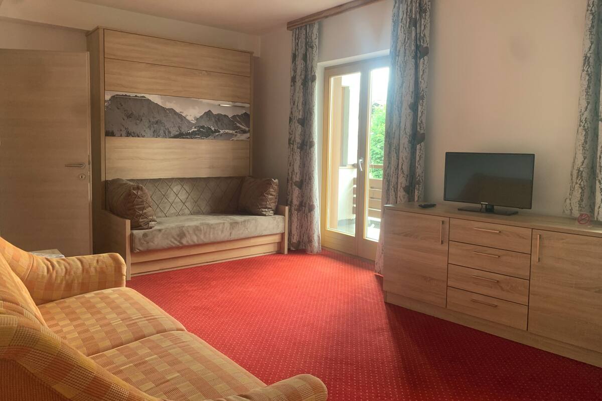 A room with a sofa, a television on a wooden cabinet, a painting on the wall, and a red carpet.