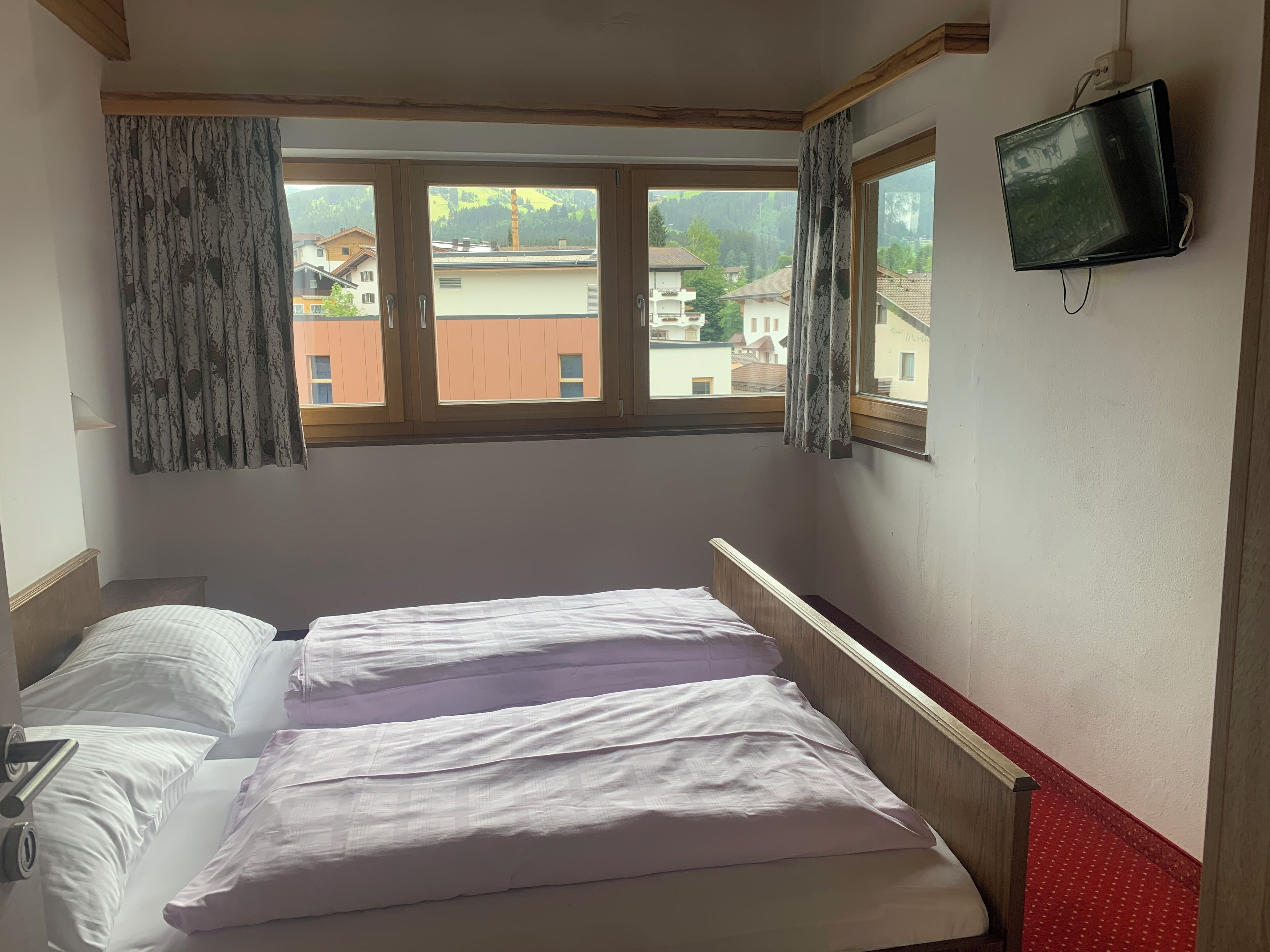 A hotel room with a bed, a TV mounted on the wall, and a window with curtains.