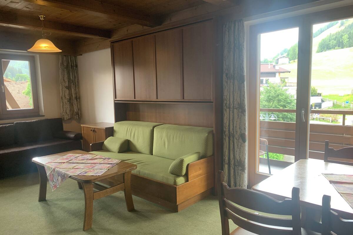 A cozy living room with a green sofa, wooden table, and a view of a balcony.