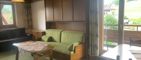 A cozy living room with a green sofa, wooden table, and a view of a balcony.