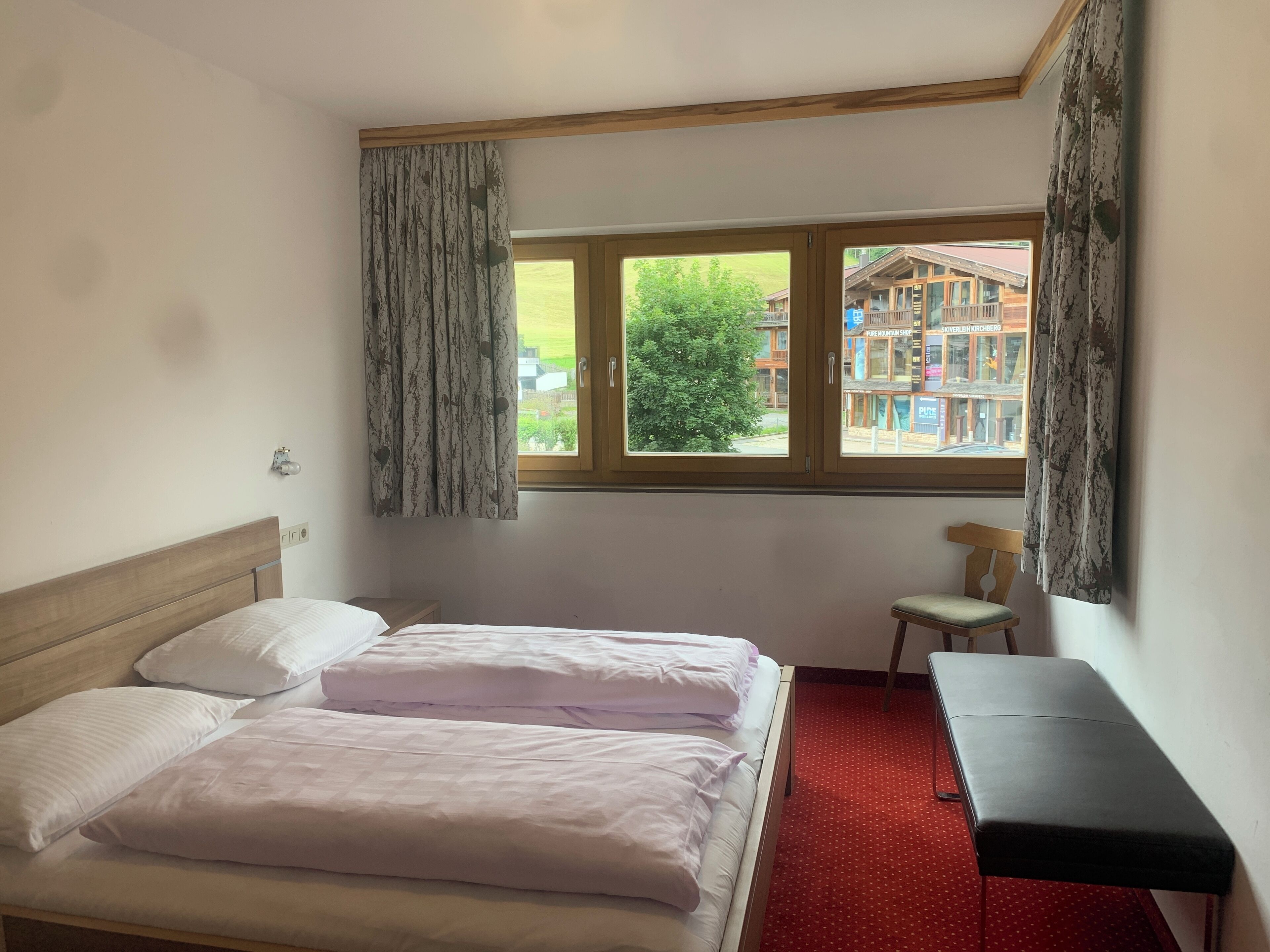 A bedroom with a bed, a small table, a chair, and a window with curtains.