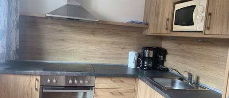 A compact kitchen with wooden cabinets, a stainless steel oven, a microwave, a coffee maker, and a sink.