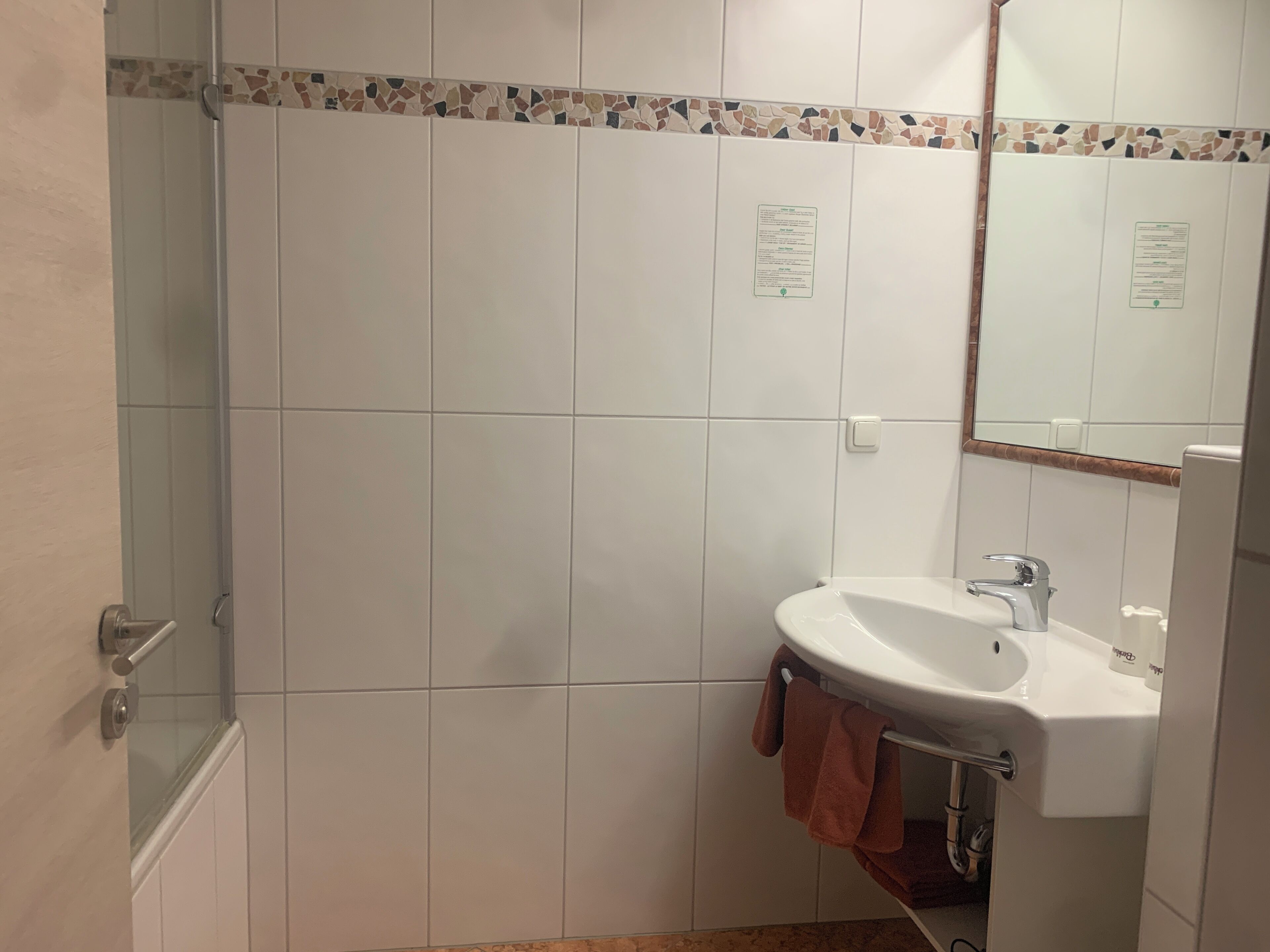 A bathroom with white tiles, a glass shower enclosure, a sink with a faucet, and a towel hanging on the wall.