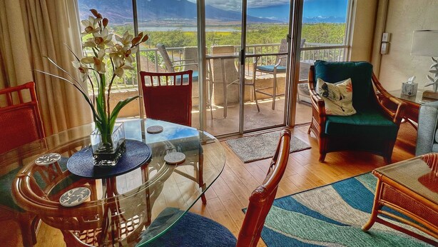 A room with a glass table, chairs, a sofa, and a view of mountains through large windows. - Ocean Sanctuary Beachfront 1-bedroom Kihei, Maui (Kihei)