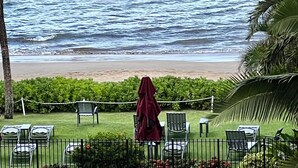 A pool area with a view of the ocean, a canoe, and outdoor seating. - Ocean Sanctuary Beachfront 1-bedroom Kihei, Maui (Kihei)