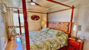 A four-poster bed with a floral bedspread, a wooden nightstand with a lamp, and a wall-mounted artwork. - Ocean Sanctuary Beachfront 1-bedroom Kihei, Maui (Kihei)