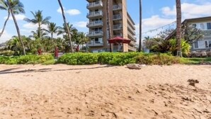 A beachfront hotel with multiple floors, palm trees, and a sandy beach. - Ocean Sanctuary Beachfront 1-bedroom Kihei, Maui (Kihei)