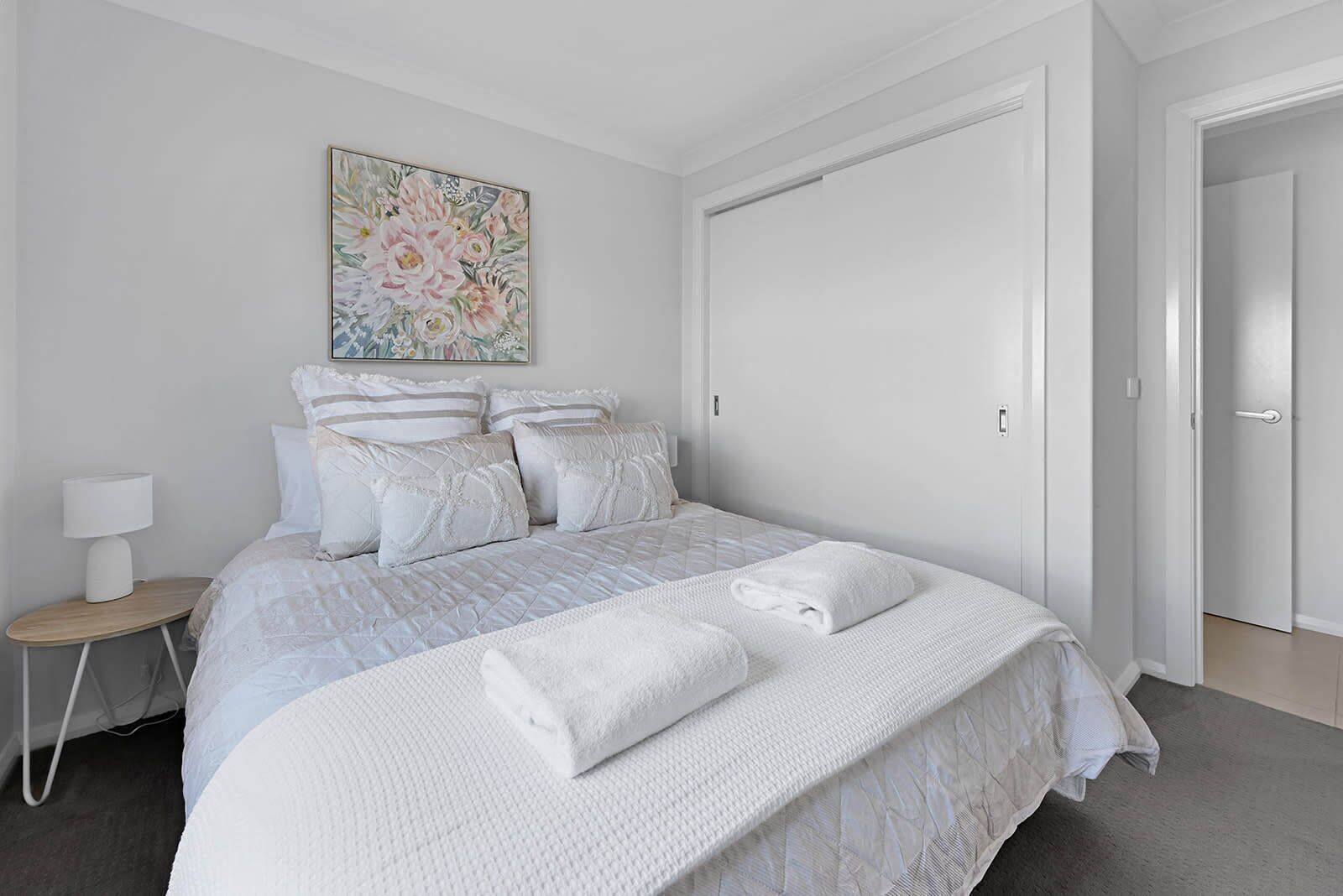 Un dormitorio con cama, almohadas, una mesita de noche, una lámpara y una puerta.
