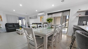 Un salon moderne avec une table à manger en verre, des canapés gris et un coin cuisine doté d’un plan de travail gris.