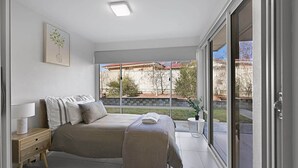 Une chambre à coucher avec un lit, une table de chevet, une lampe et une vue sur l’extérieur.