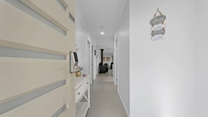 Un couloir avec une porte blanche, une enseigne fixée au mur et une petite plante posée sur une étagère.