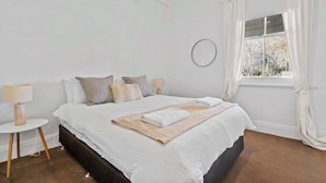 Un dormitorio con una cama grande, dos mesitas de noche, un ventanal con cortinas y vistas a árboles.